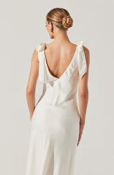 A woman wearing a sleeveless, cream-colored satin dress with a deep V back and shoulder ties. The fabric appears smooth and shiny, giving an elegant and sophisticated look.